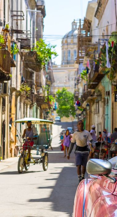 Typischer Oldtimer geparkt in einer sonnigen und belebten Gasse in der Altstadt von Havanna